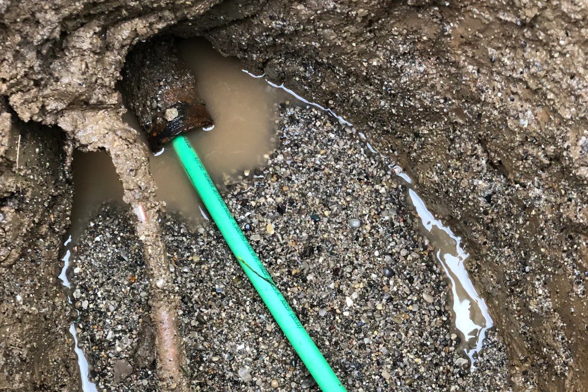 A green pipe is in the dirt near water.